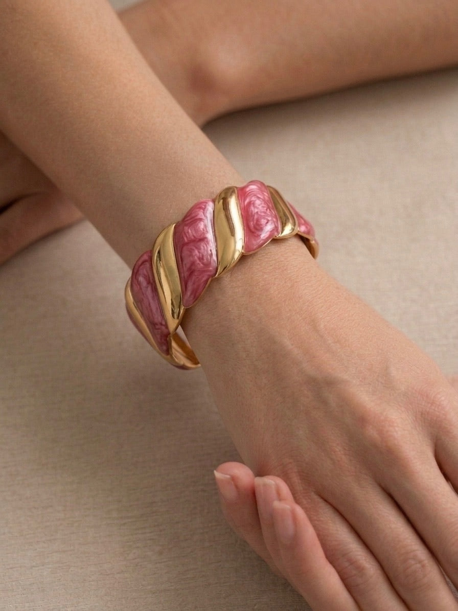 bracelet manchette torsadé en métal doré et maillons effet nacre rose porté au poignet