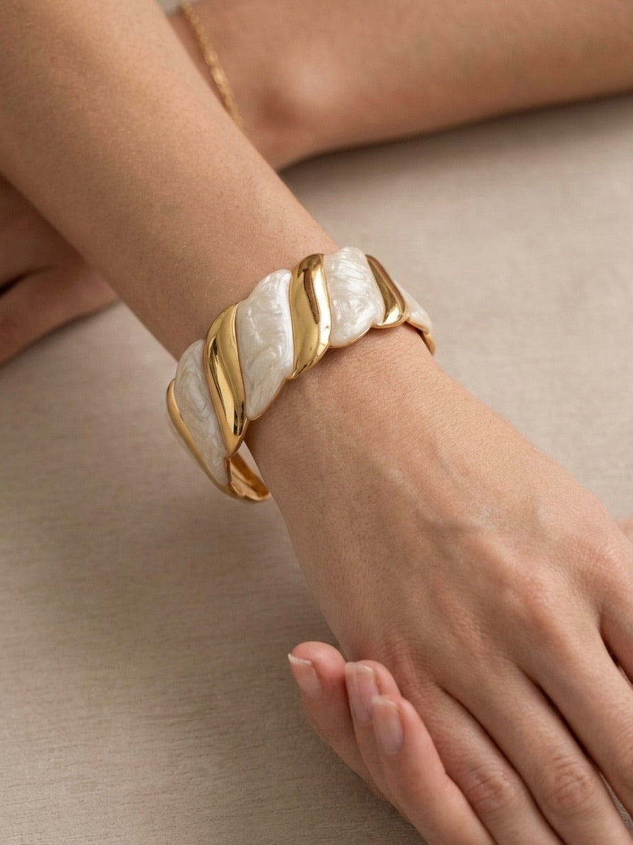 bracelet manchette torsadé en métal doré et maillons effet nacre blanc porté au poignet.