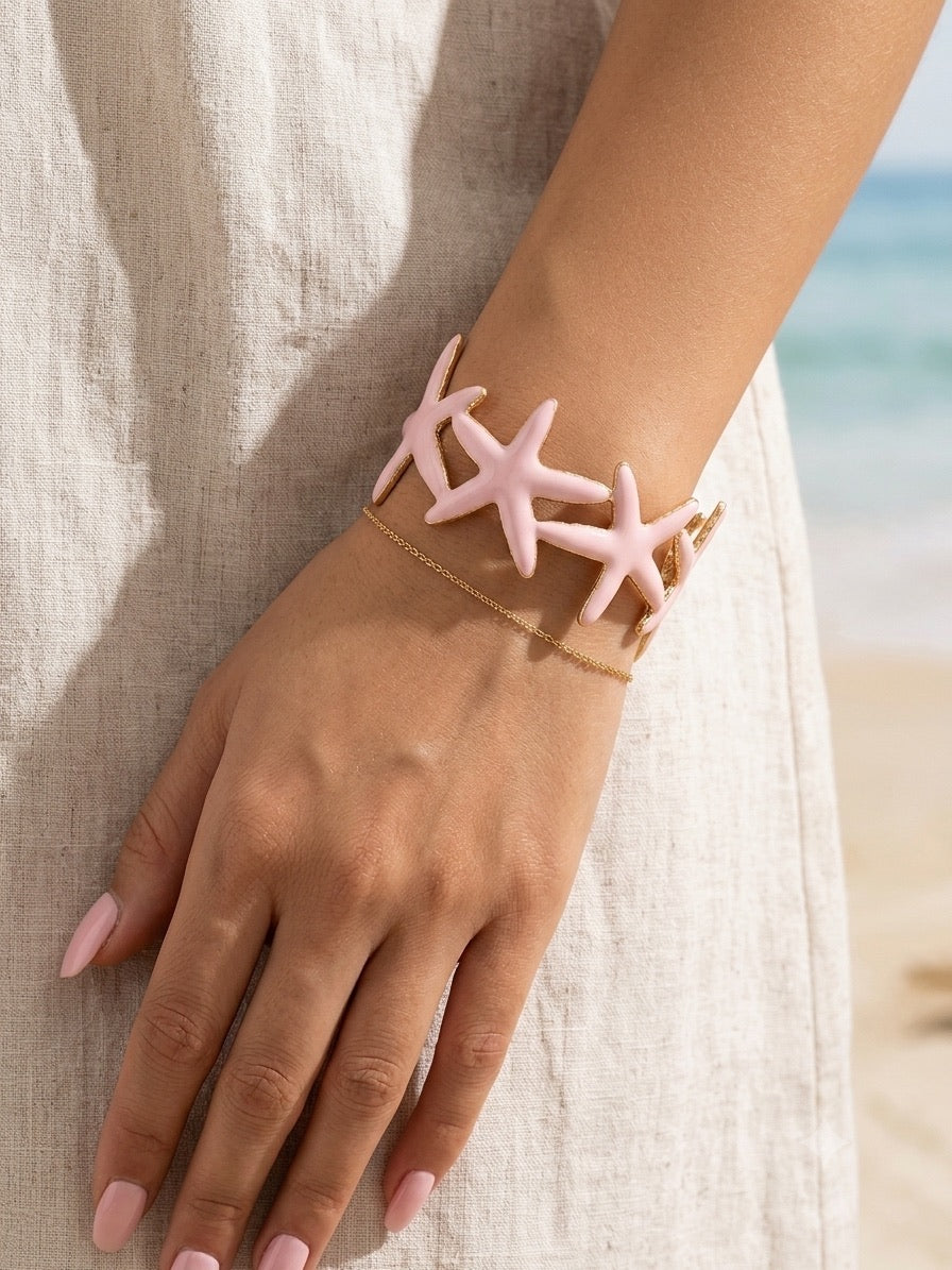 bracelet manchette à motifs étoiles de mer rose poudré et doré porté au poignet.